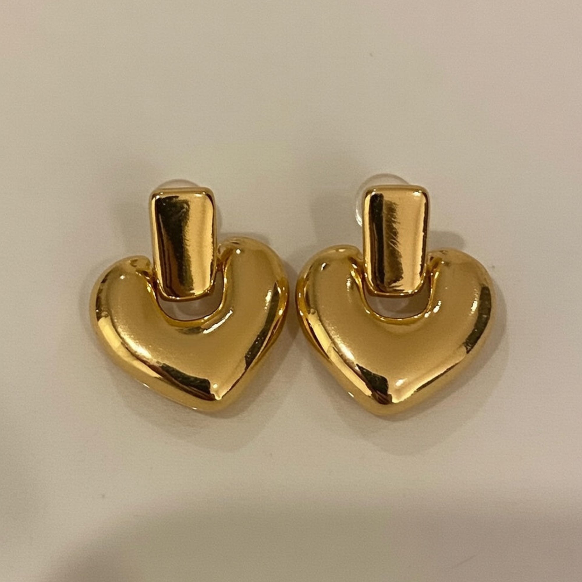 Pair of gold heart-shaped earrings on a light beige background