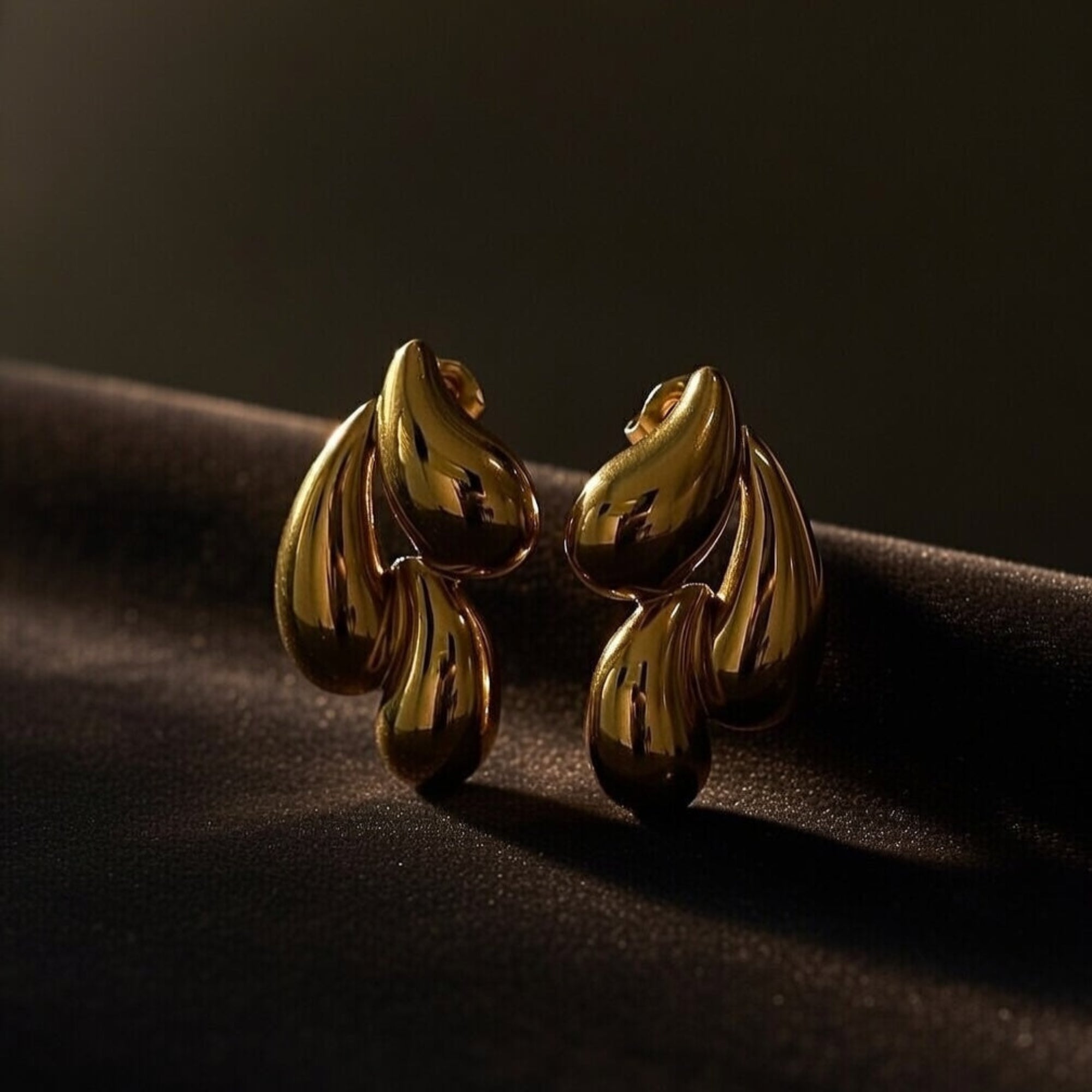 Gold leaf earrings on a dark fabric background