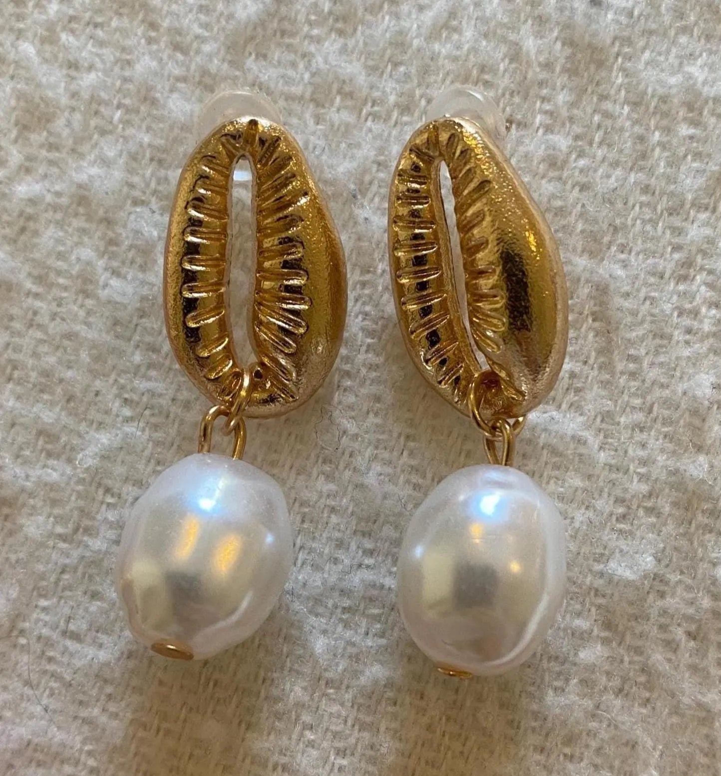 Gold earrings with pearl drops on a textured beige background