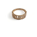 A gold ring with a wide band featuring a geometric pattern paved with small clear gemstone stones, luxury design