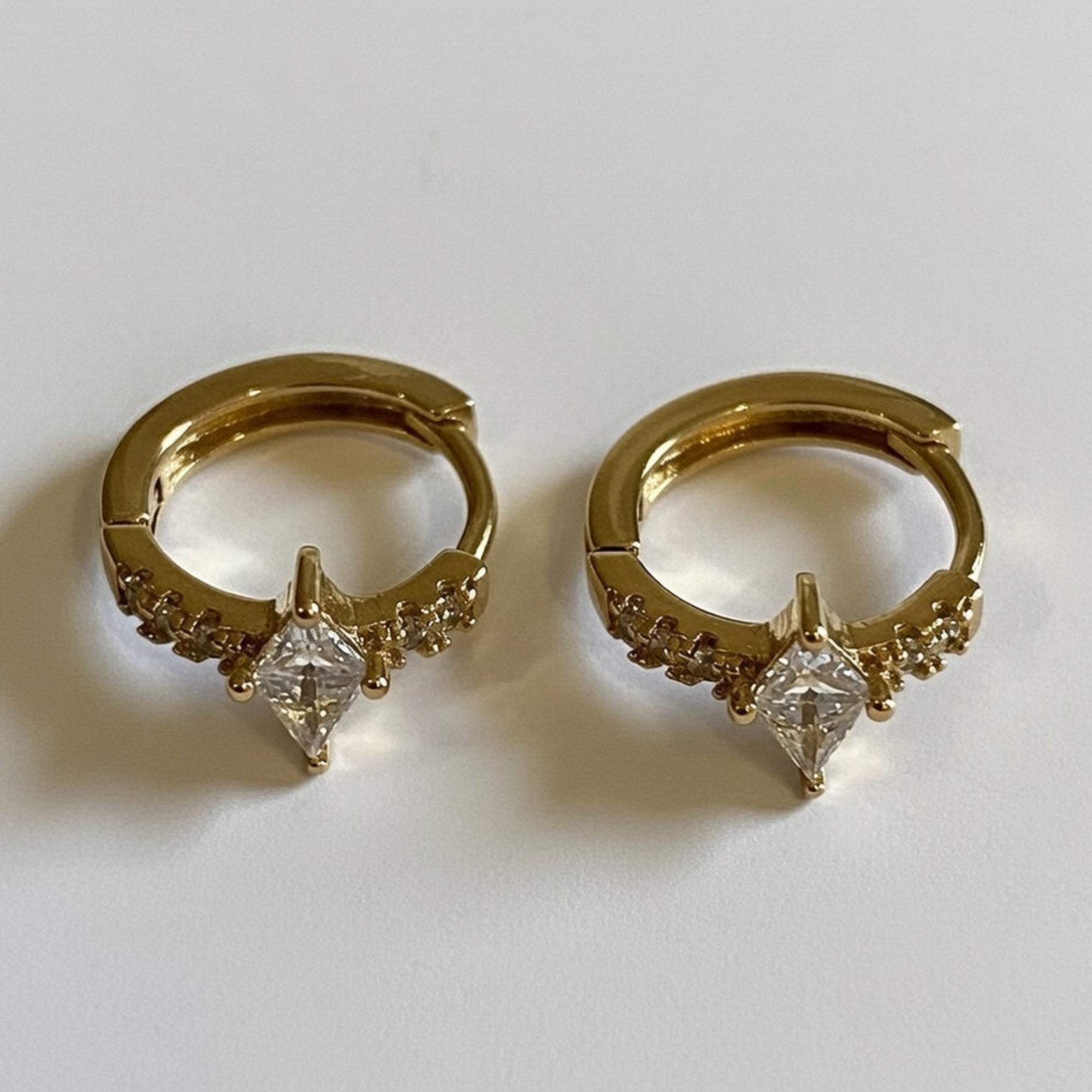Gold hoop earrings with diamond-like stones on a white background
