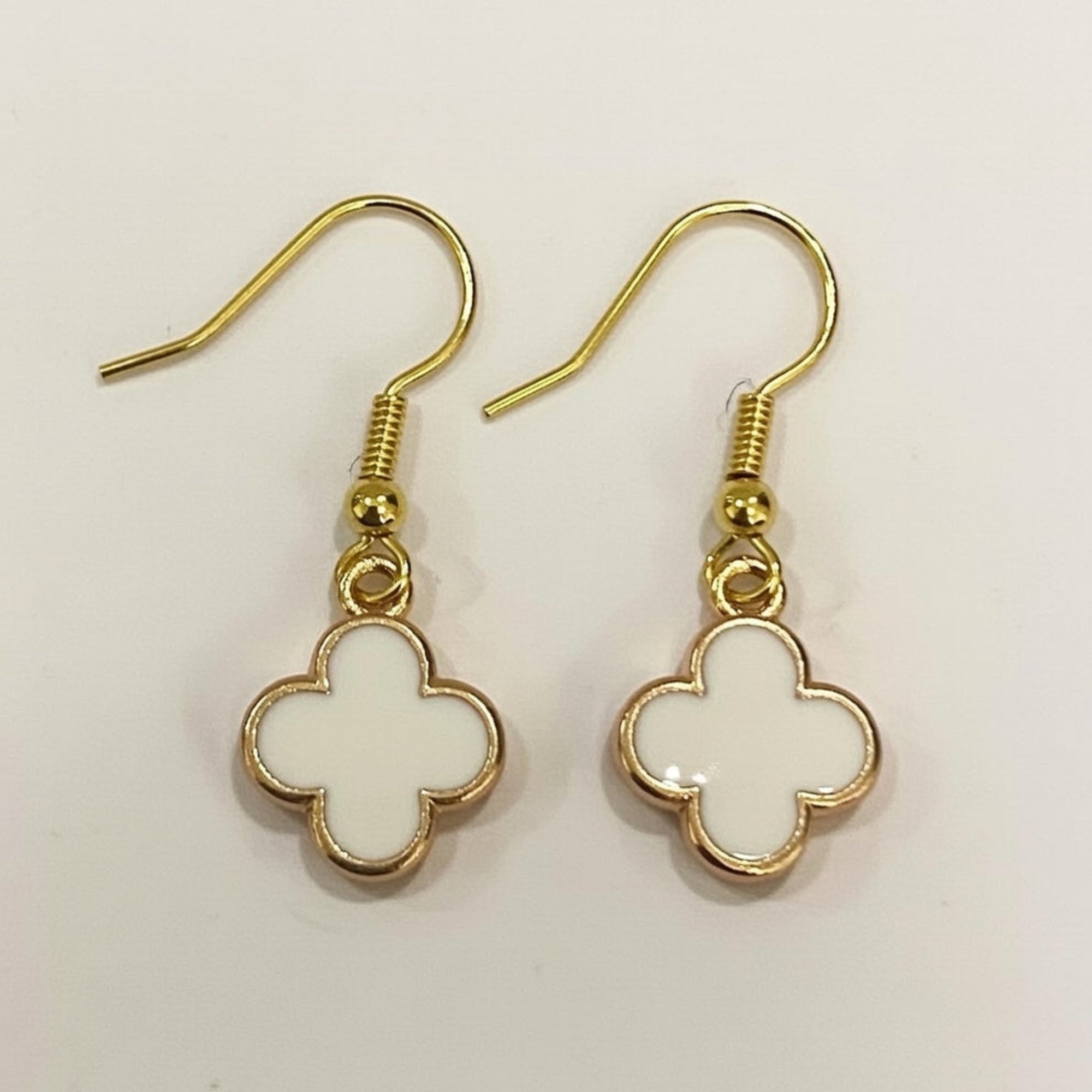 Gold and white clover-shaped earrings on a light background