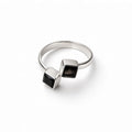 A silver ring featuring two square bezel-set black gemstones on a plain white background.